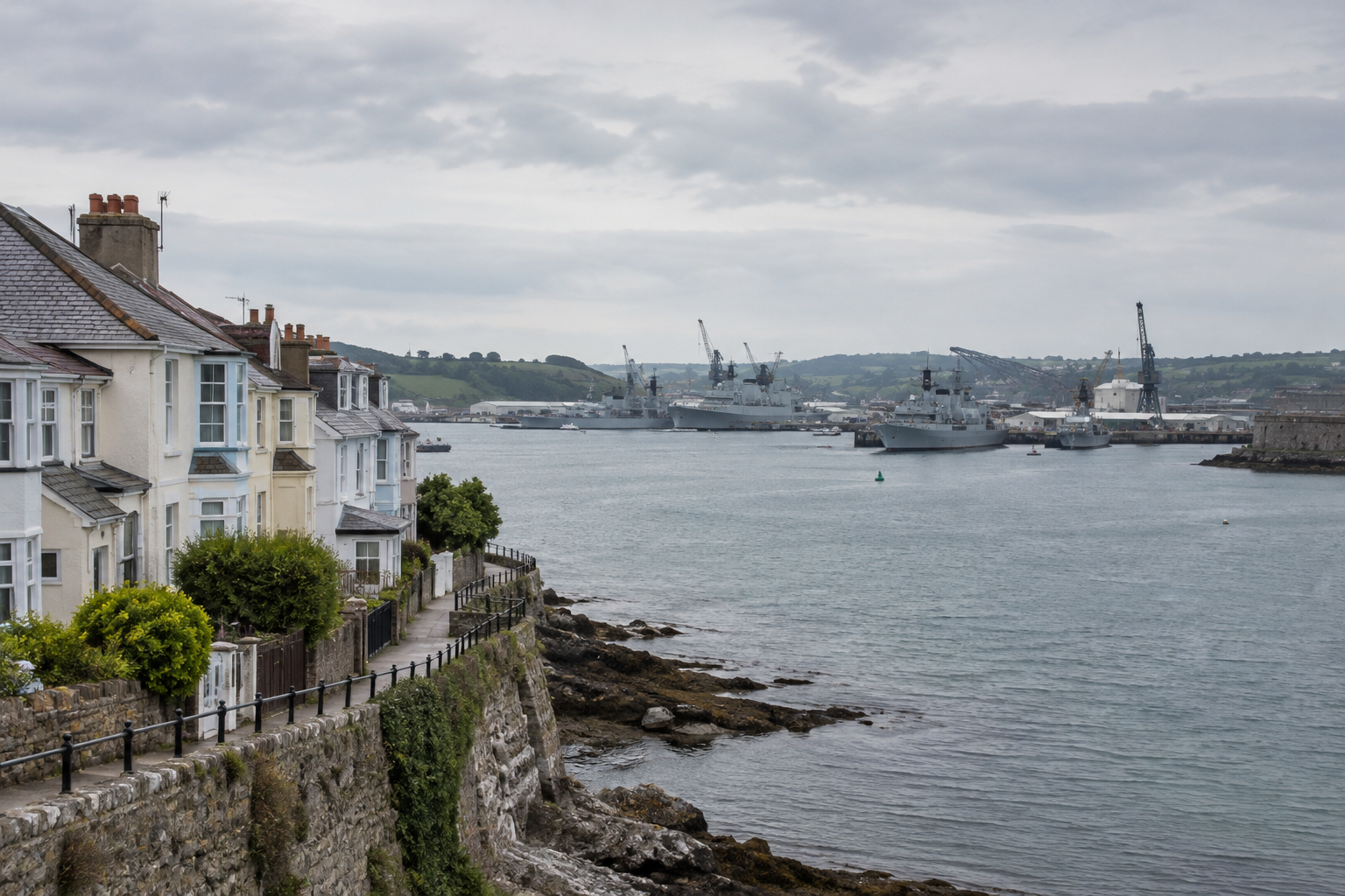 Plymouth waterfront in Devon with homes and distant naval dockyard infrastructure under an overcast sky